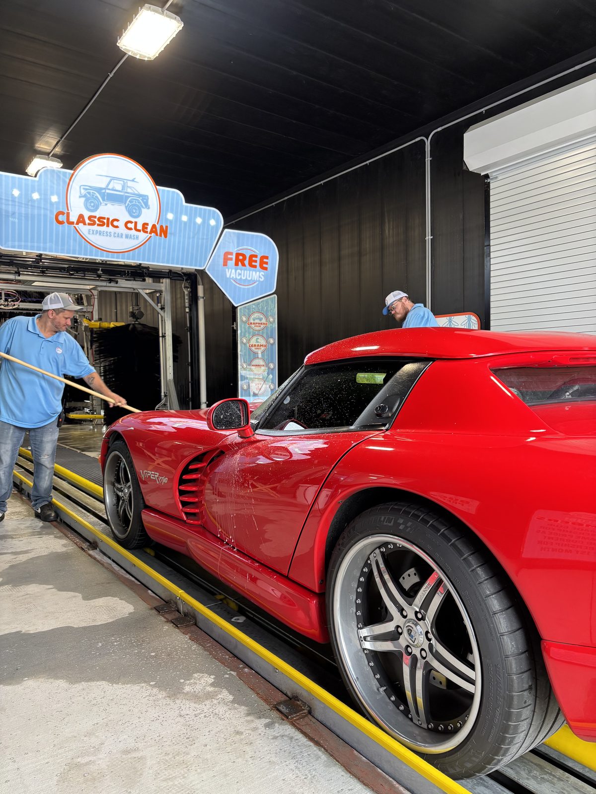 Two Classic Clean team members hand-prepping a red sports car at the tunnel entrance
