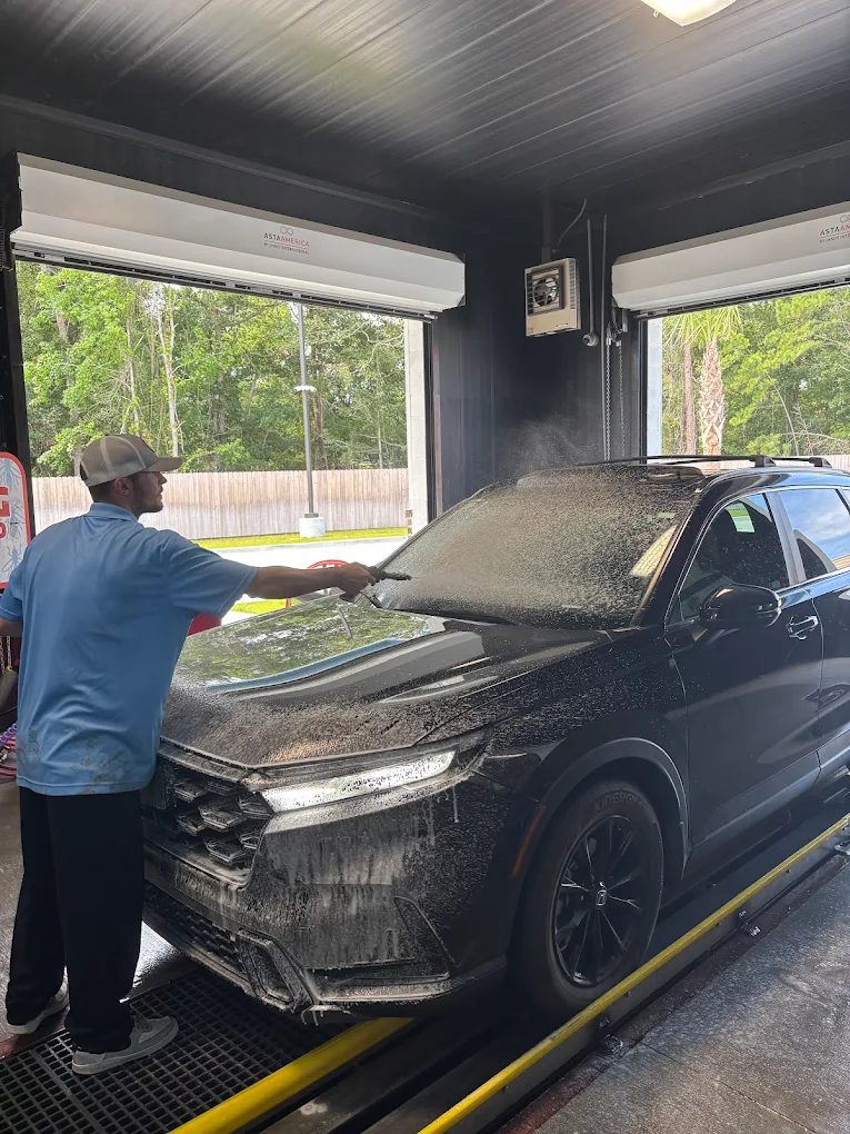 A Classic Clean team member hand-prepping an SUV before it enters the tunnel